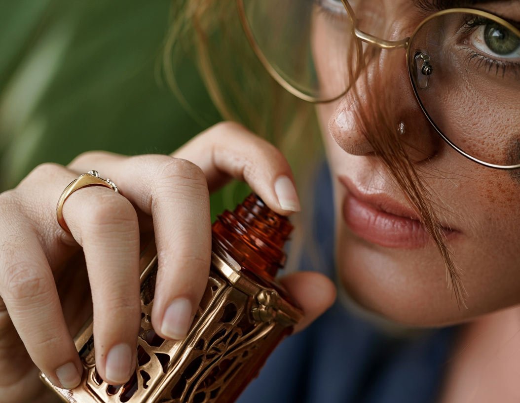 Person smelling oud oil from an ornate perfume bottle